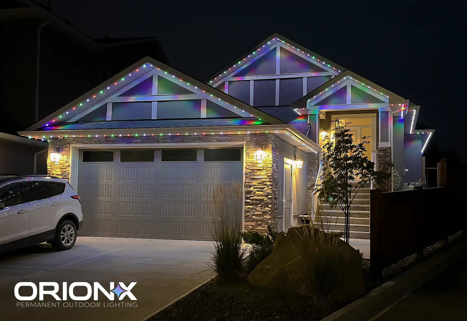 Home at night with OrionX permanent roofline lighting glowing in multicolour