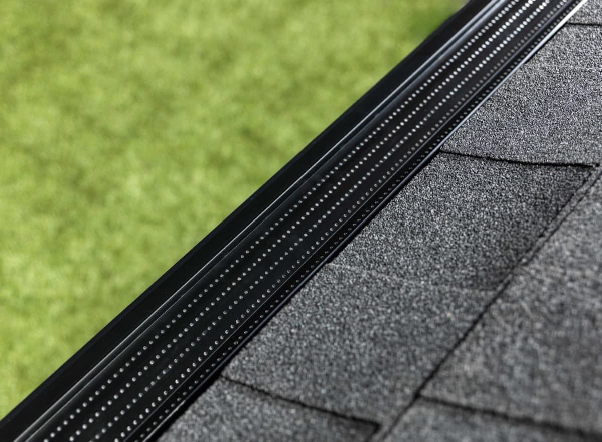Low-profile black gutter guard installed flush under the shingle line, seen from above